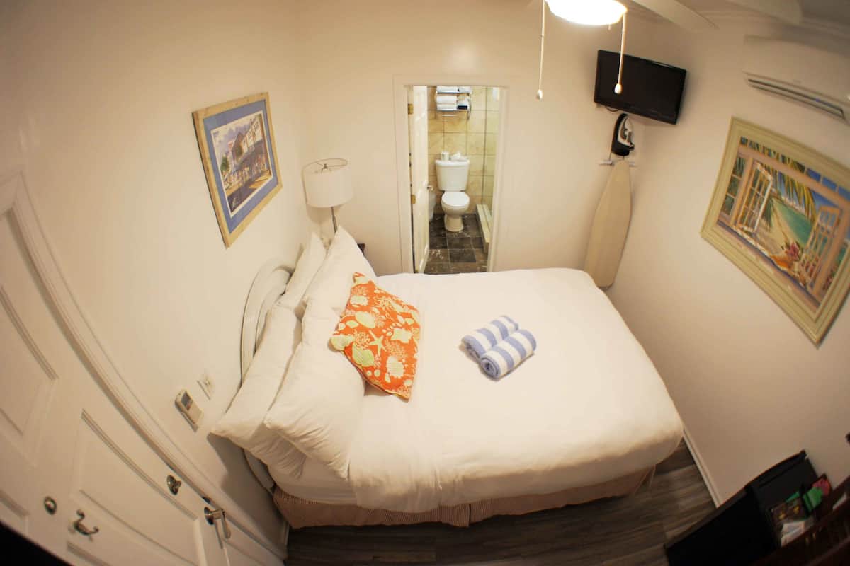 Ein Hotelzimmer mit einem Bett, einer Nachttischlampe, einem an der Wand befestigten Fernseher und einer Tür zu einem Badezimmer.