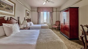 Habitación de hotel con dos camas, un armario, ventilador de techo y ventana con cortinas.