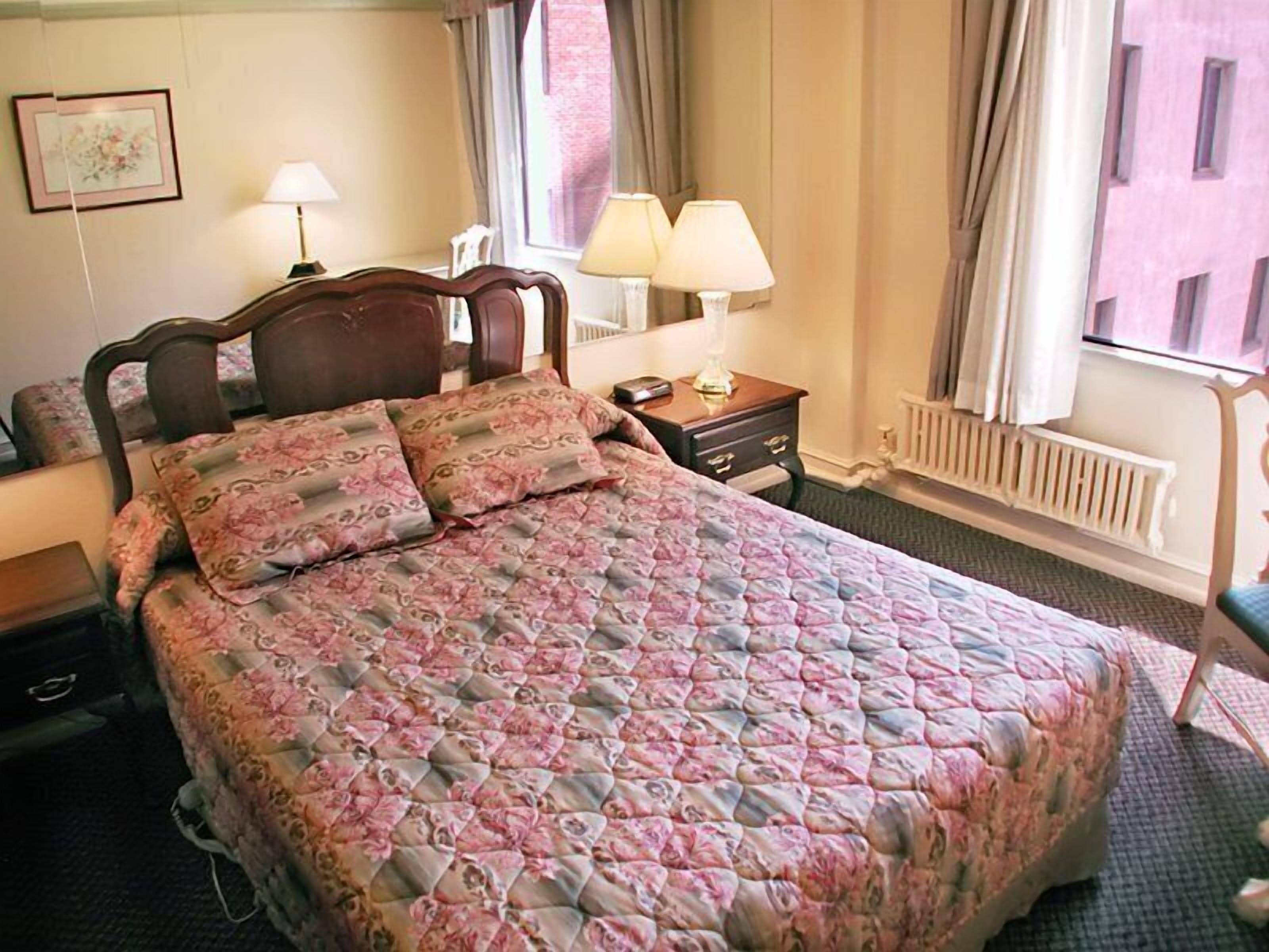 Habitación de hotel con una cama grande, dos lámparas de noche, una mesita de noche, un aparador y una ventana con cortinas.