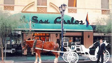 Un carruaje tirado por caballos frente a un edificio con un letrero que dice 'San Carlos'.