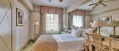 A hotel room with a large bed, a ceiling fan, a desk, a chair, and a mirror.