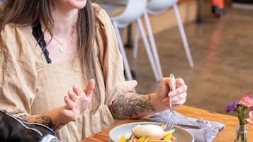 Una persona sentada en una mesa de madera con platos de comida, una taza de café y un florero con flores.