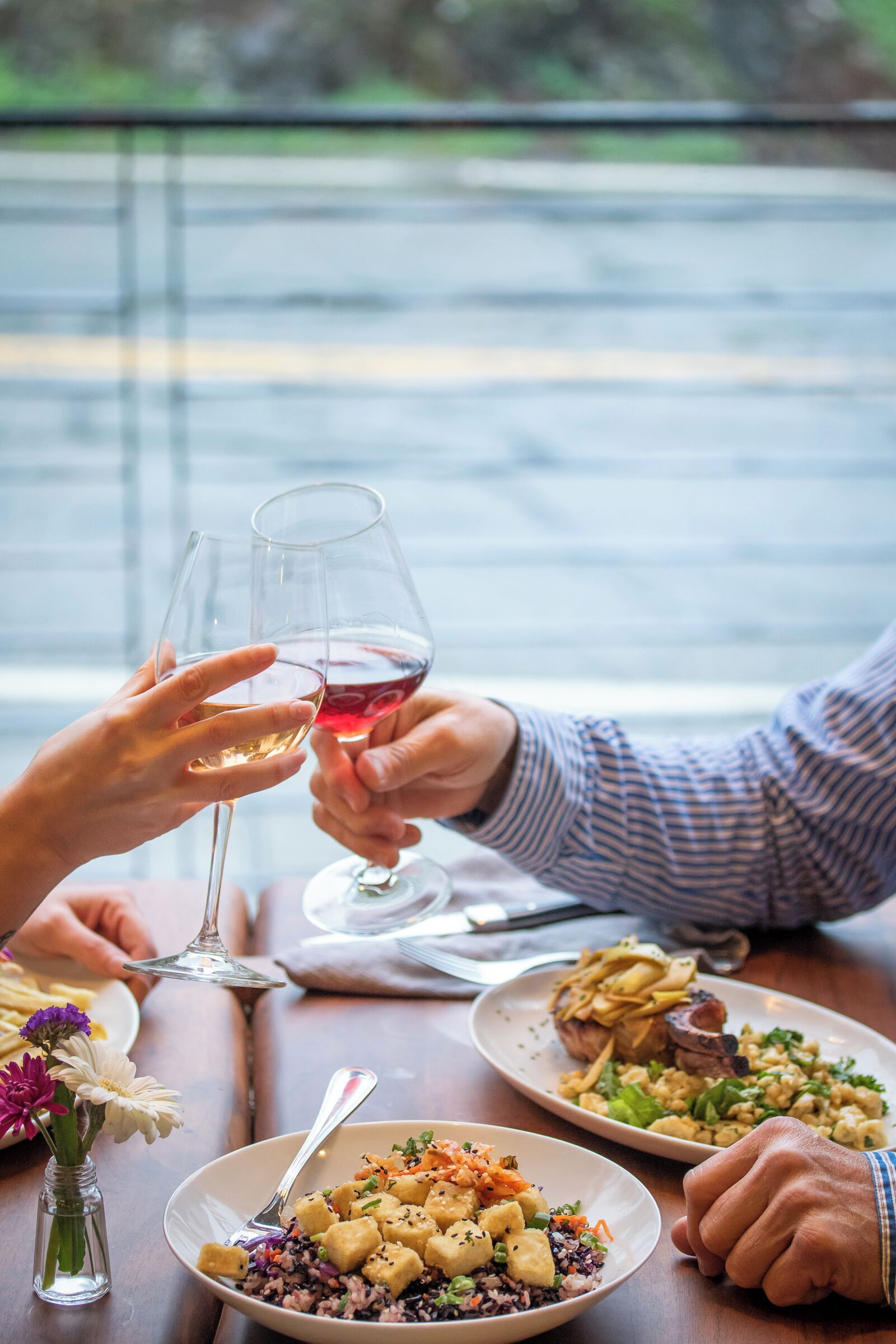 Una mesa de comedor con platos de comida, copas de vino y un jarrón con flores.