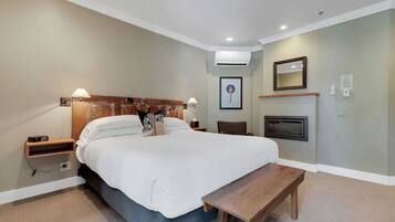A bedroom with a bed, bedside tables, a bench, an air conditioning unit, a fireplace, and a framed picture on the wall.