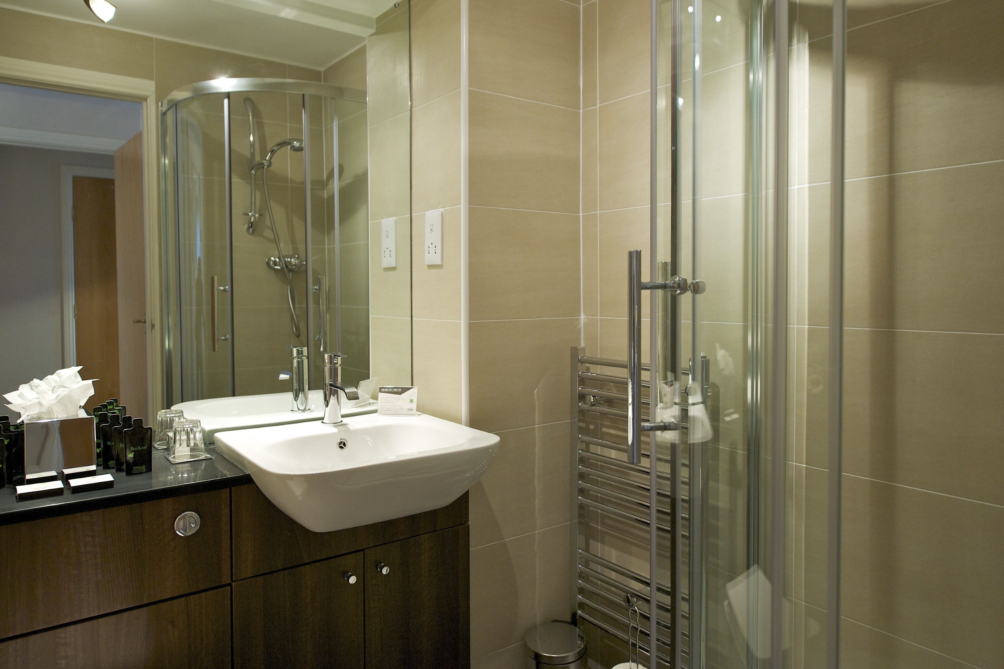 Een moderne badkamer met een douchecabine van glas, een wastafel met dubbele wastafel en een spiegel boven de wastafel.