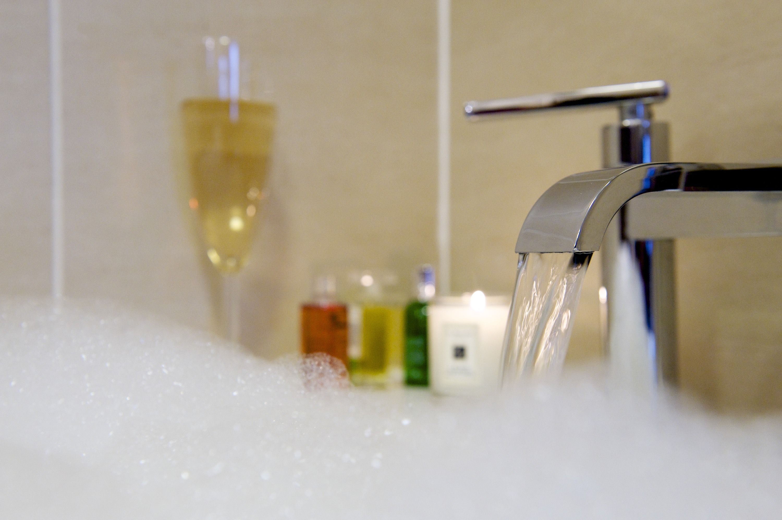 A bathroom with a running faucet, a glass of liquid, and toiletries on the counter.