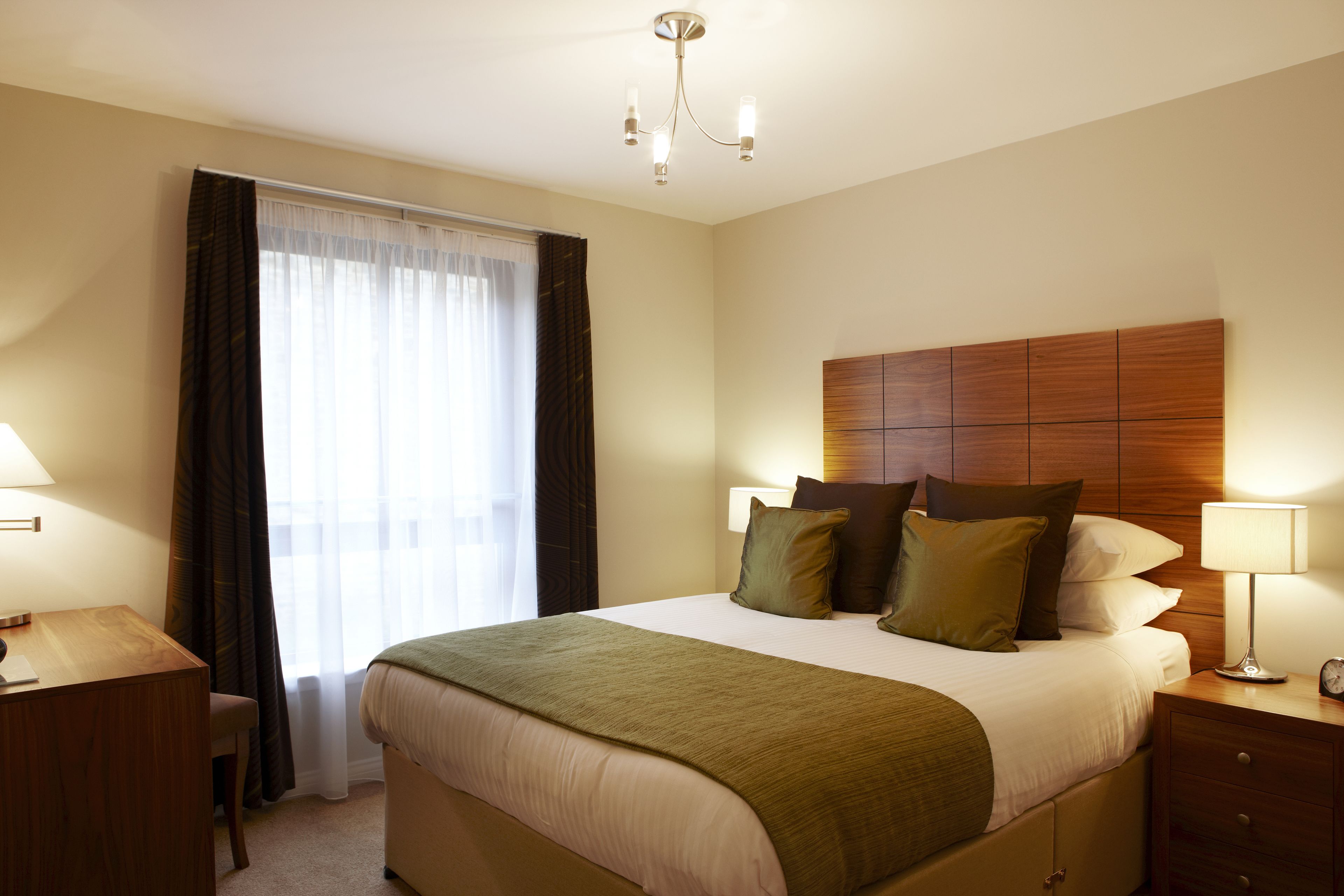 A hotel room with a bed, bedside tables, a desk, and a window with curtains.