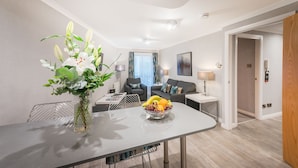 Ett modernt vardagsrum med ett matbord, en vas med blommor och en fruktskål. Det finns två soffor, ett soffbord och en lampa.