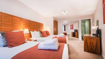 A hotel room with two beds, a wooden headboard, a desk with a television, and a bathroom visible through an open door.