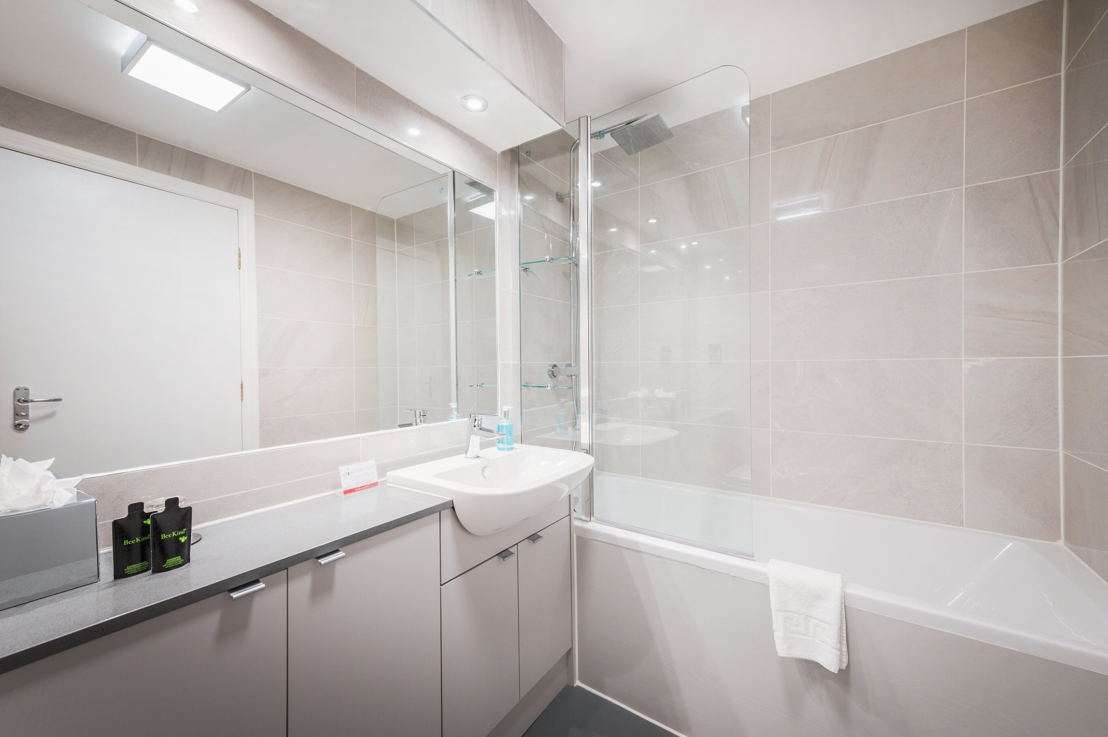 Een moderne badkamer met een douchecabine van glas, een witte wastafel en een grote spiegel.