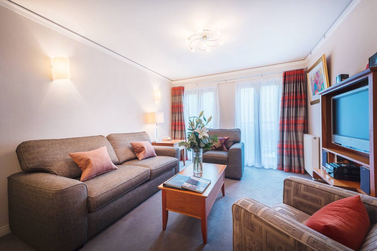 A modern living room with a sofa, armchair, coffee table, and a television.