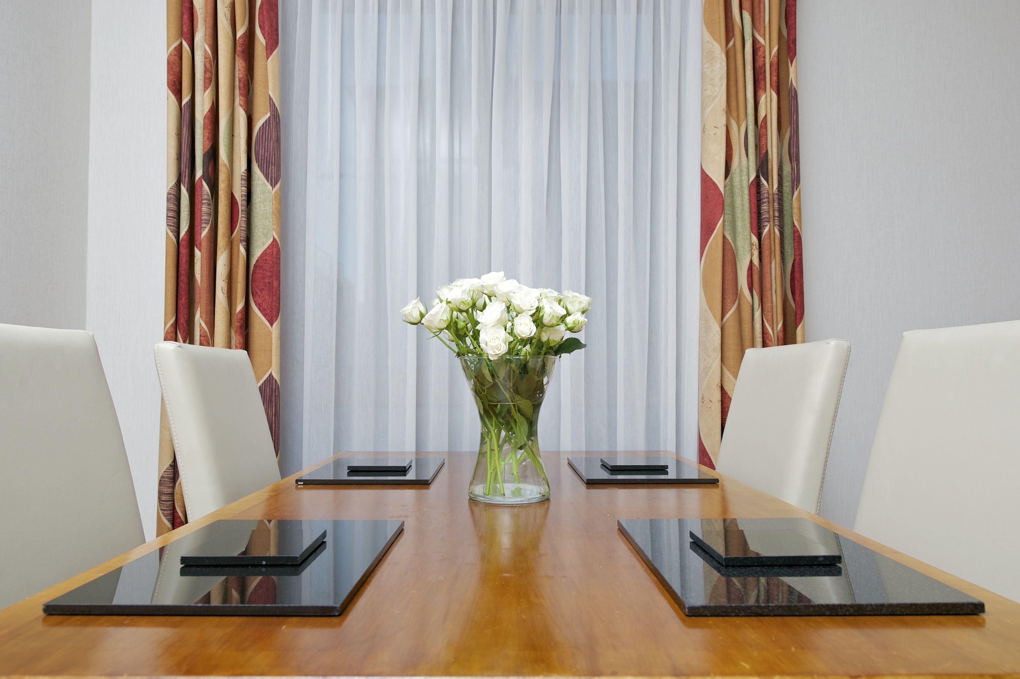 Een vergadertafel met een vaas witte bloemen in het midden, omringd door witte stoelen en zwarte tabletstandaards.