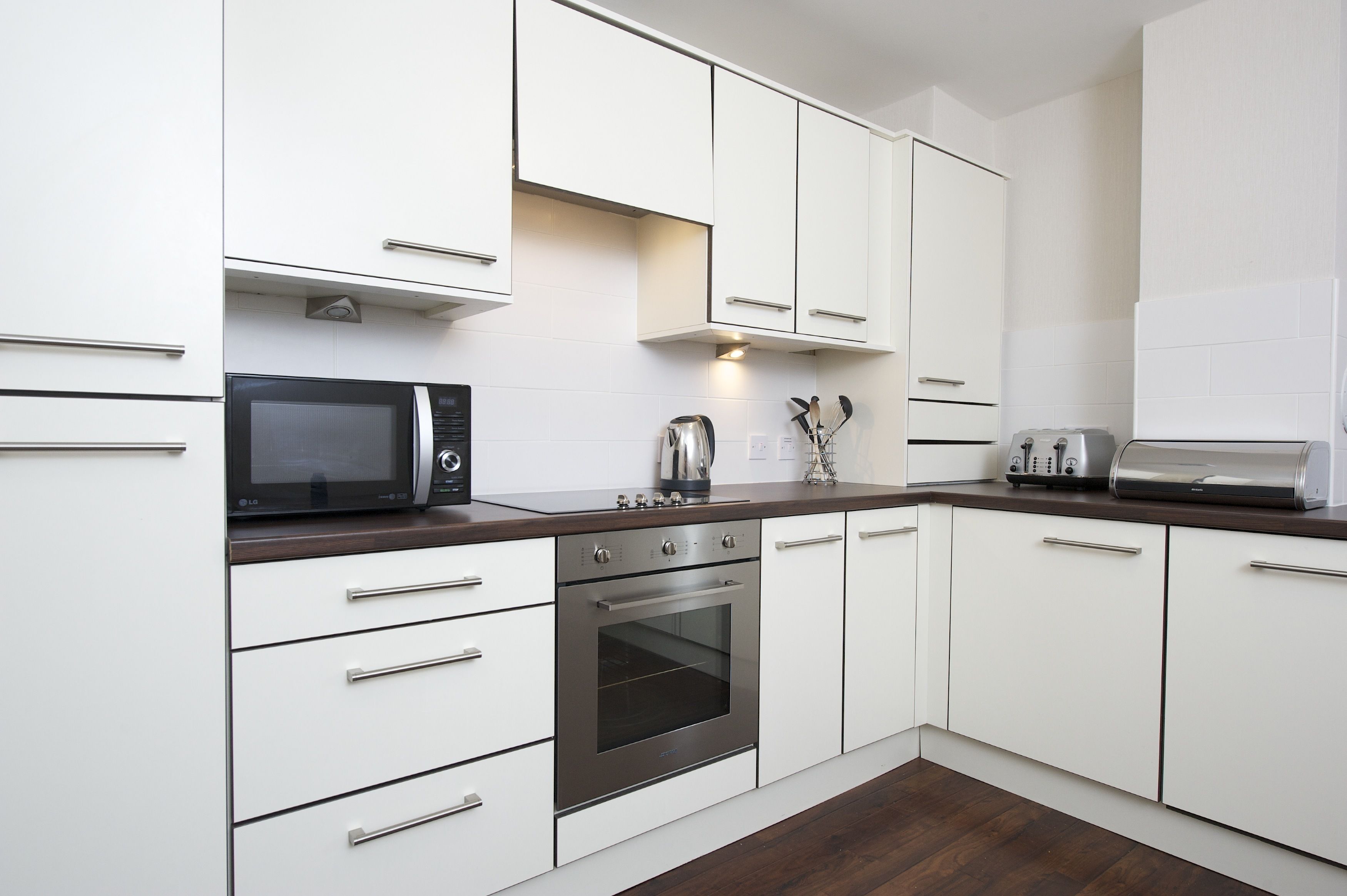 A modern kitchen with white cabinets, a stainless steel oven, a microwave, and a toaster.