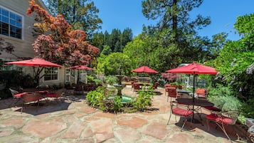Eine Terrasse mit Steinfliesen, roten Sonnenschirmen und Gartenmöbeln.