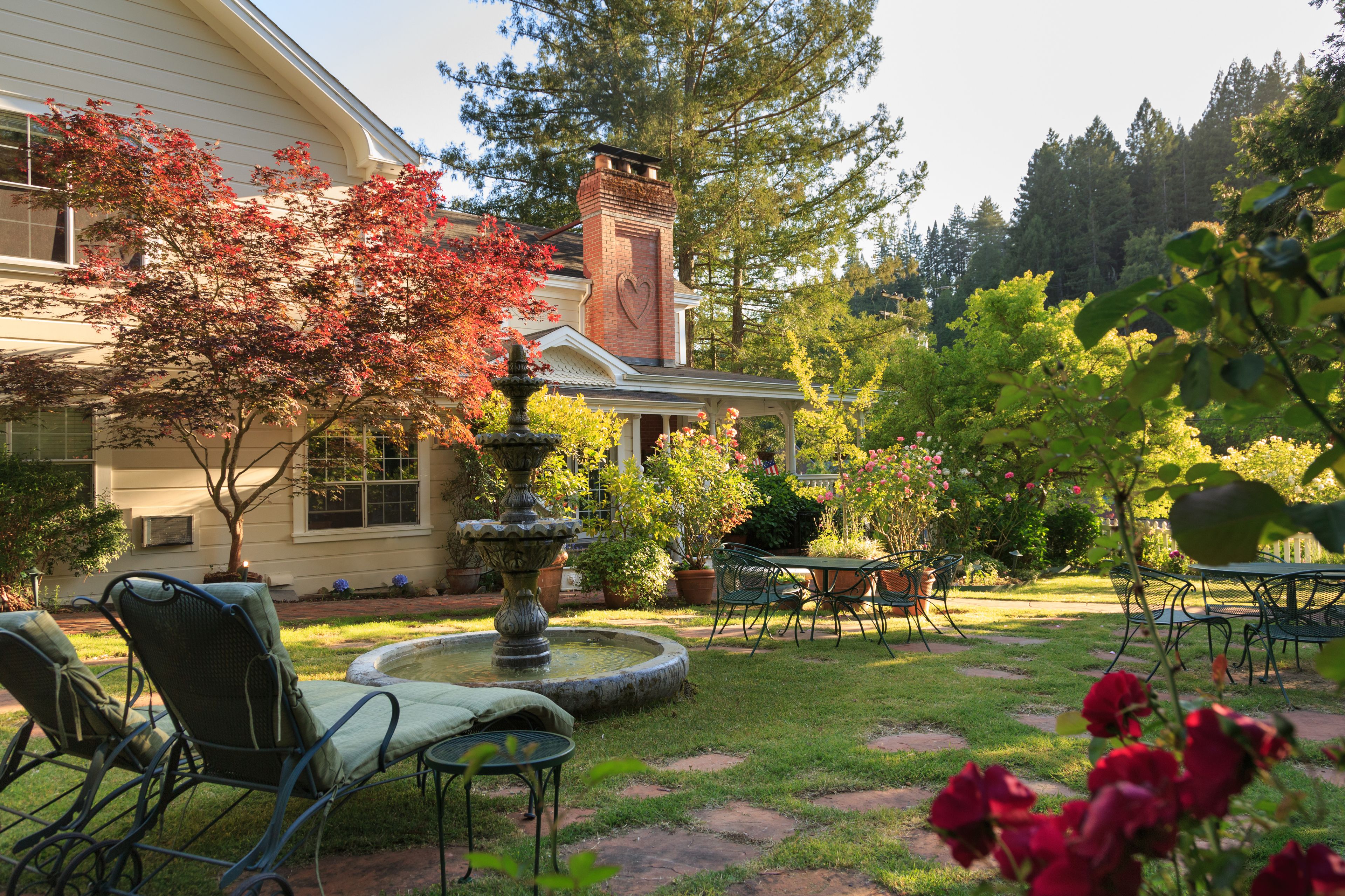 A house with a garden patio featuring a fountain, outdoor seating, and a brick chimney.
