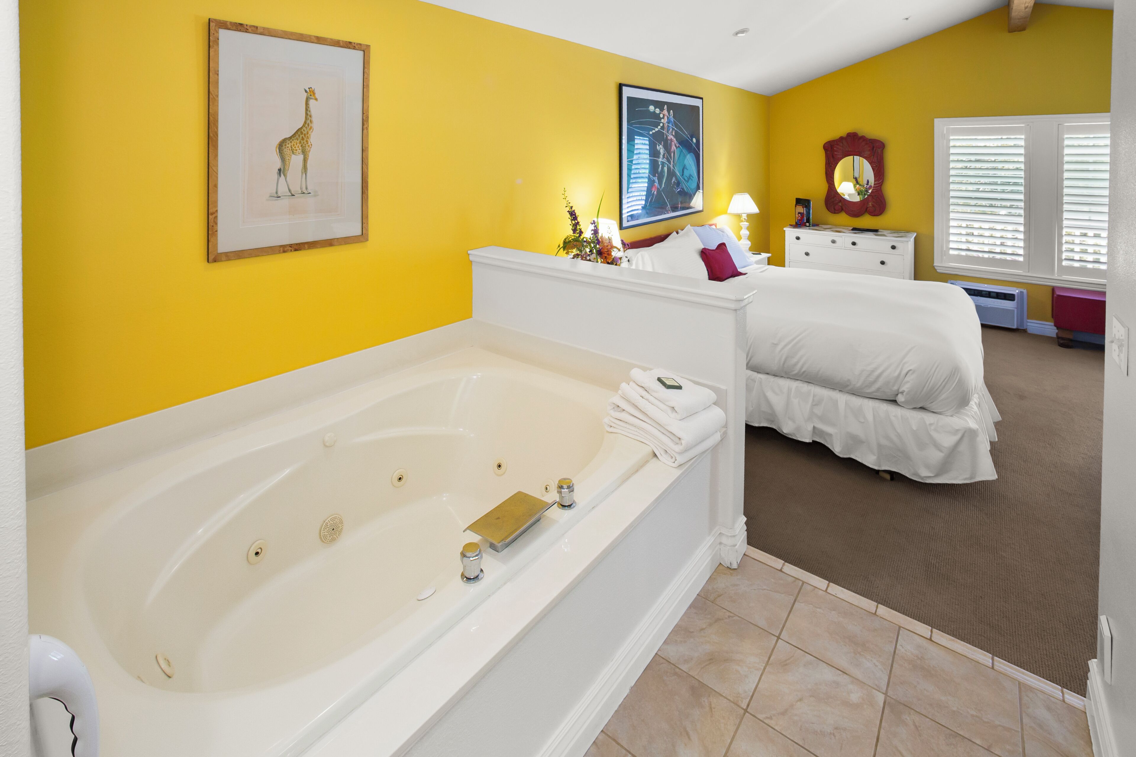 Un dormitorio con una bañera grande, una cama, un aparador y una ventana con persianas.