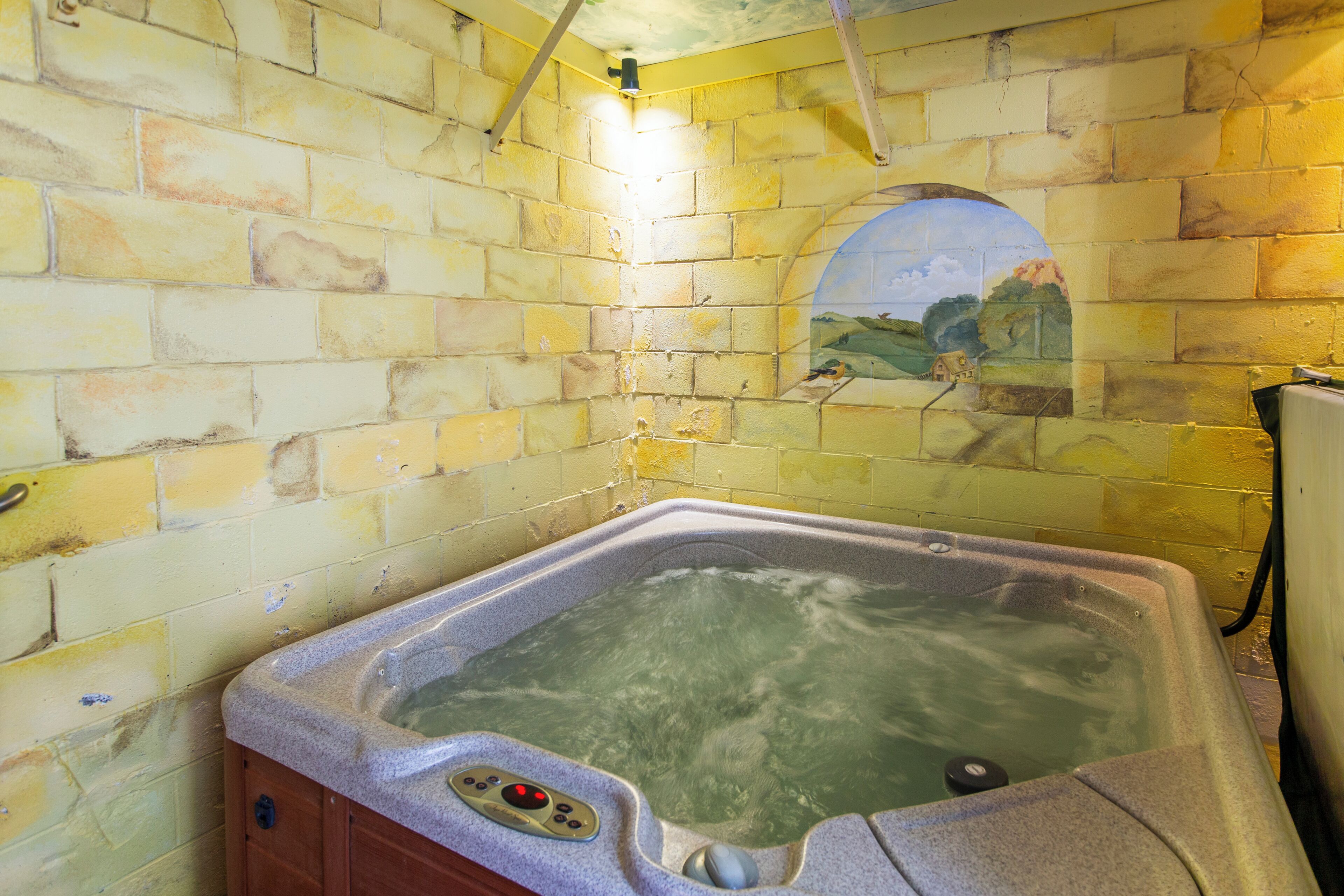A hot tub with a control panel, set against a yellow brick wall with a mural.