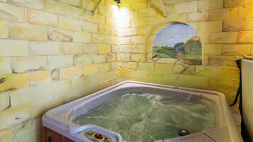 A hot tub with a control panel, set against a yellow brick wall with a mural.