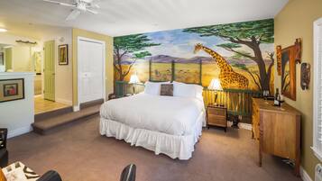 A bedroom with a large bed, a ceiling fan, a painting of a giraffe, and a nightstand with a lamp.
