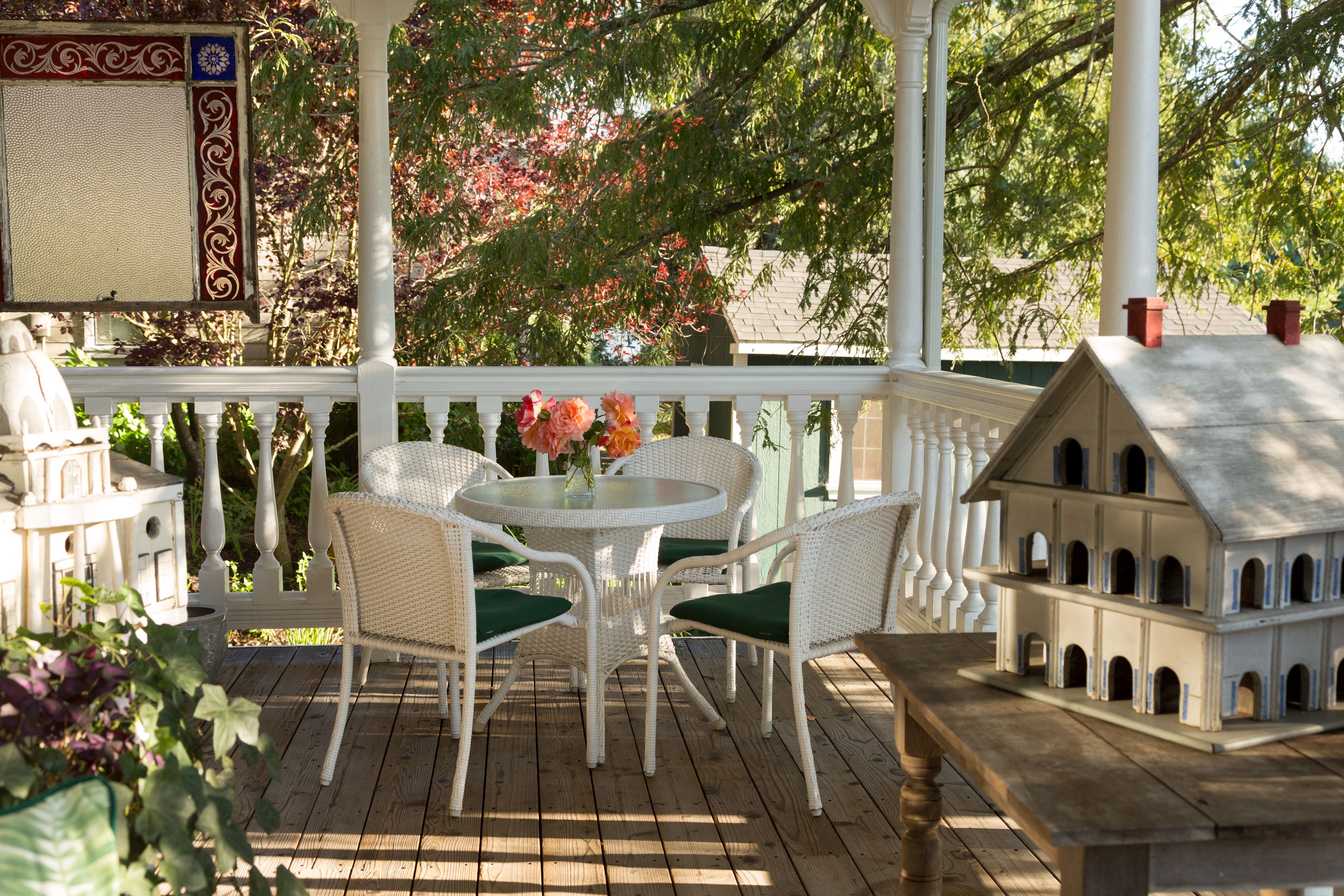 Un patio extérieur couvert avec une table ronde et des chaises, une maquette de maison et un panneau décoratif mural.