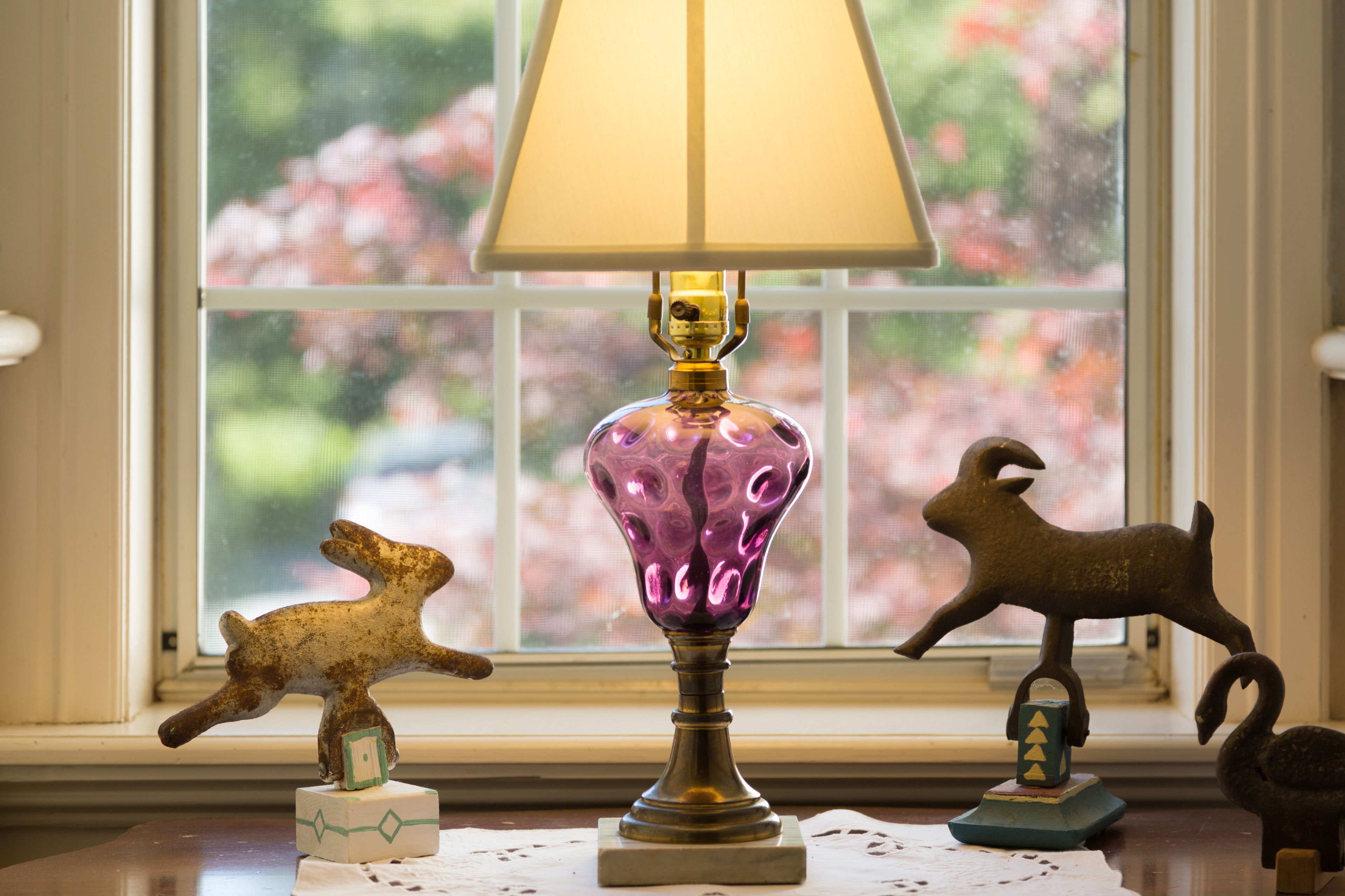 Una lámpara con pantalla decorativa, una pequeña figurina de un perro y una figurina de un caballo sobre un alféizar.