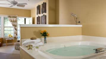 A bathroom with a large bathtub, a ceiling fan, and a window with curtains.
