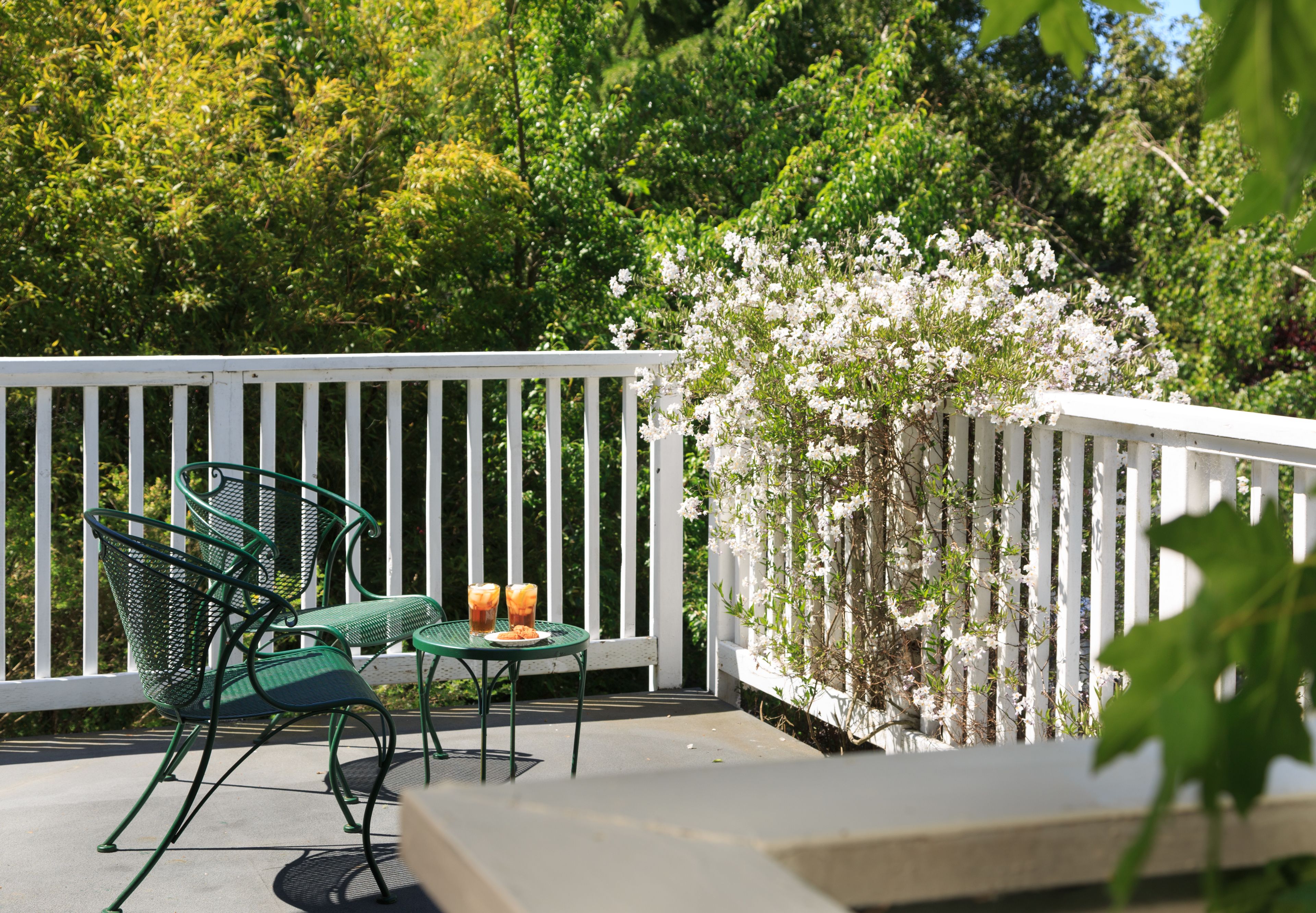 A patio with a white fence, green metal chairs, and a table with two drinks.