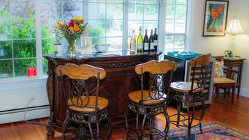 A bar area with a wooden counter, two bar stools, a vase with flowers, and bottles of wine.