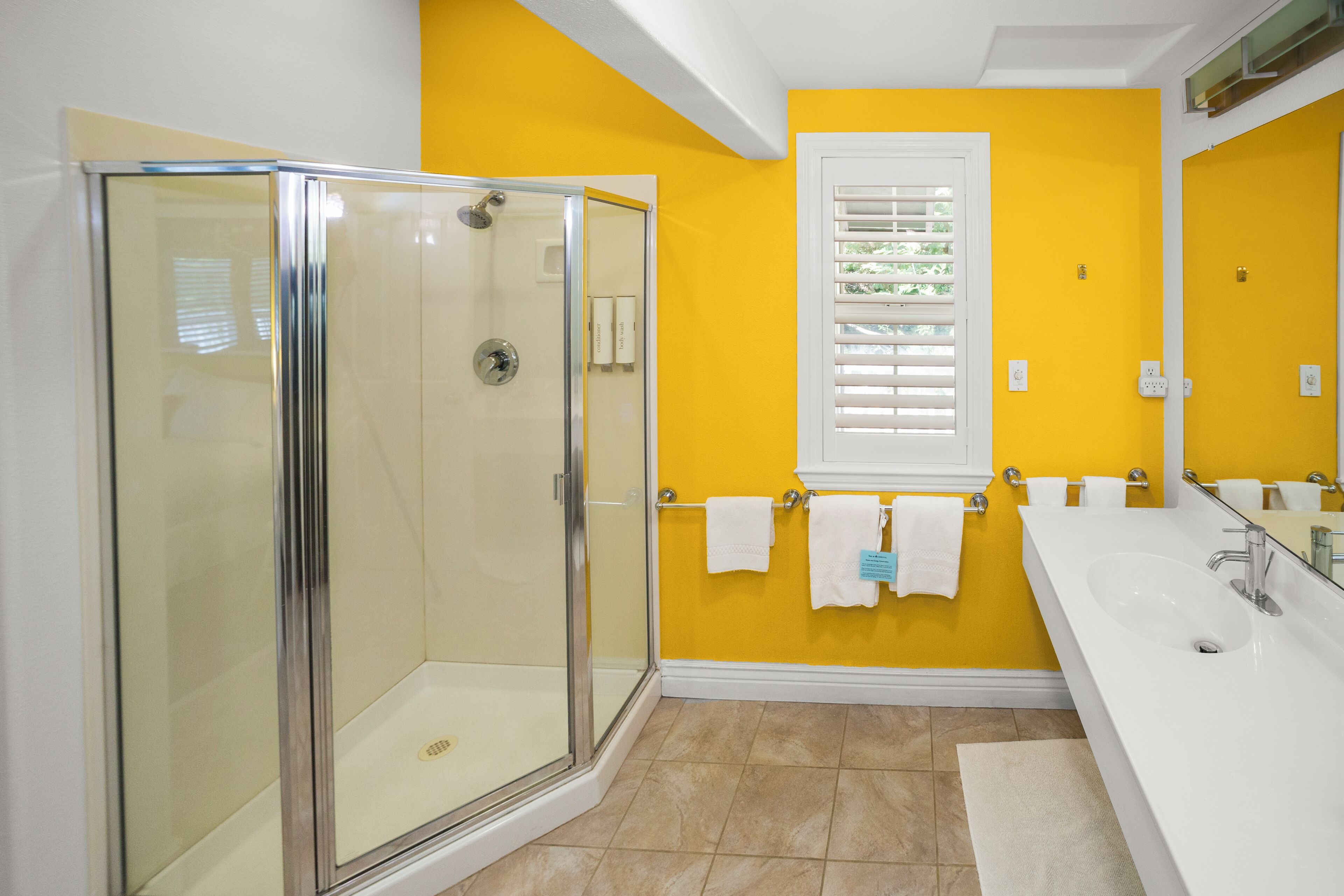 A bathroom with a glass shower enclosure, a white sink, and a yellow wall.