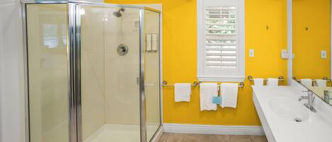 A bathroom with a glass shower enclosure, a white sink, and a yellow wall.