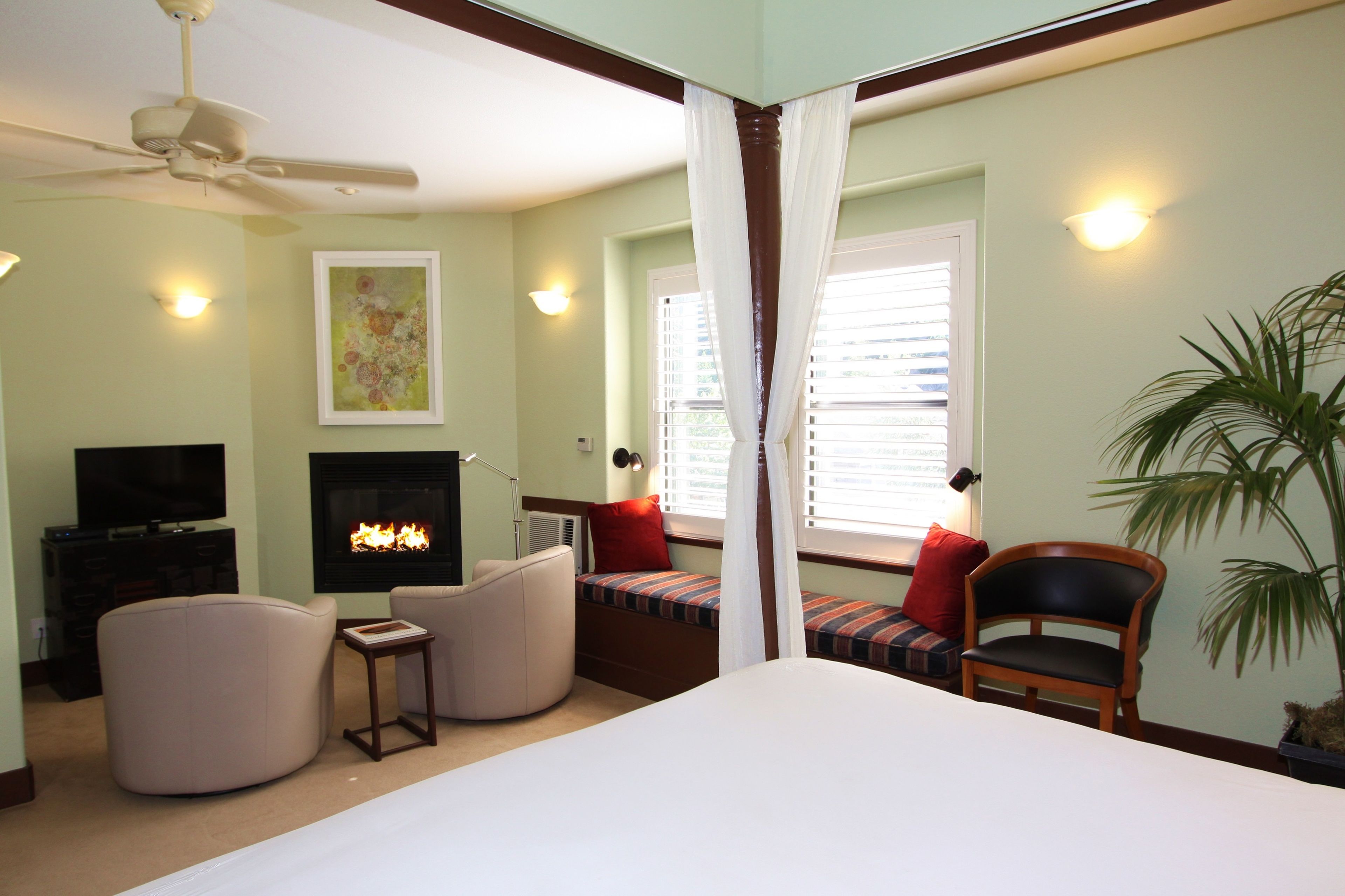 A bedroom with a bed, a TV, a fireplace, and a window with blinds.