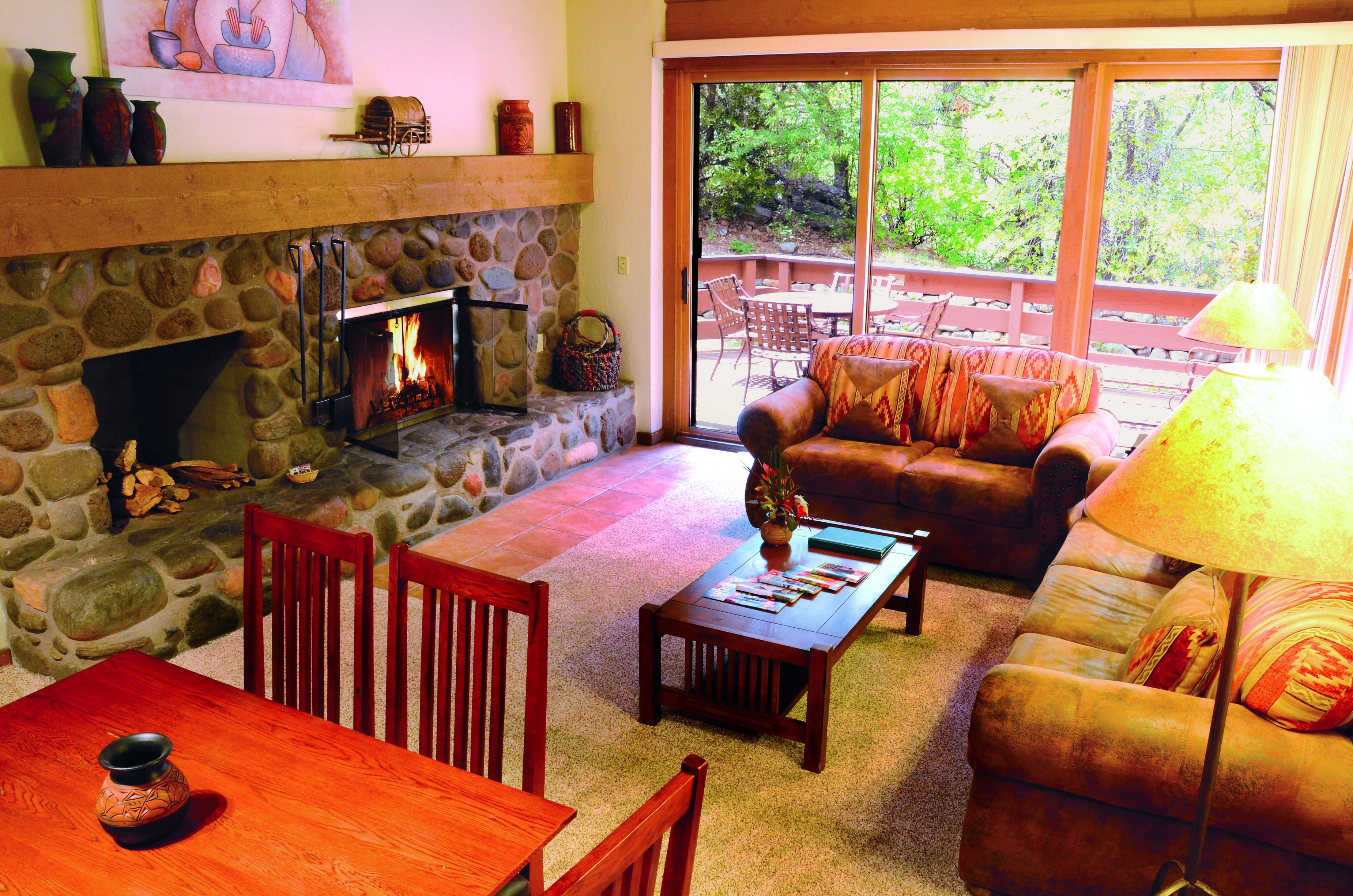 A cozy living room with a stone fireplace, a wooden coffee table, a leather sofa, and a dining area with a wooden table and chairs.