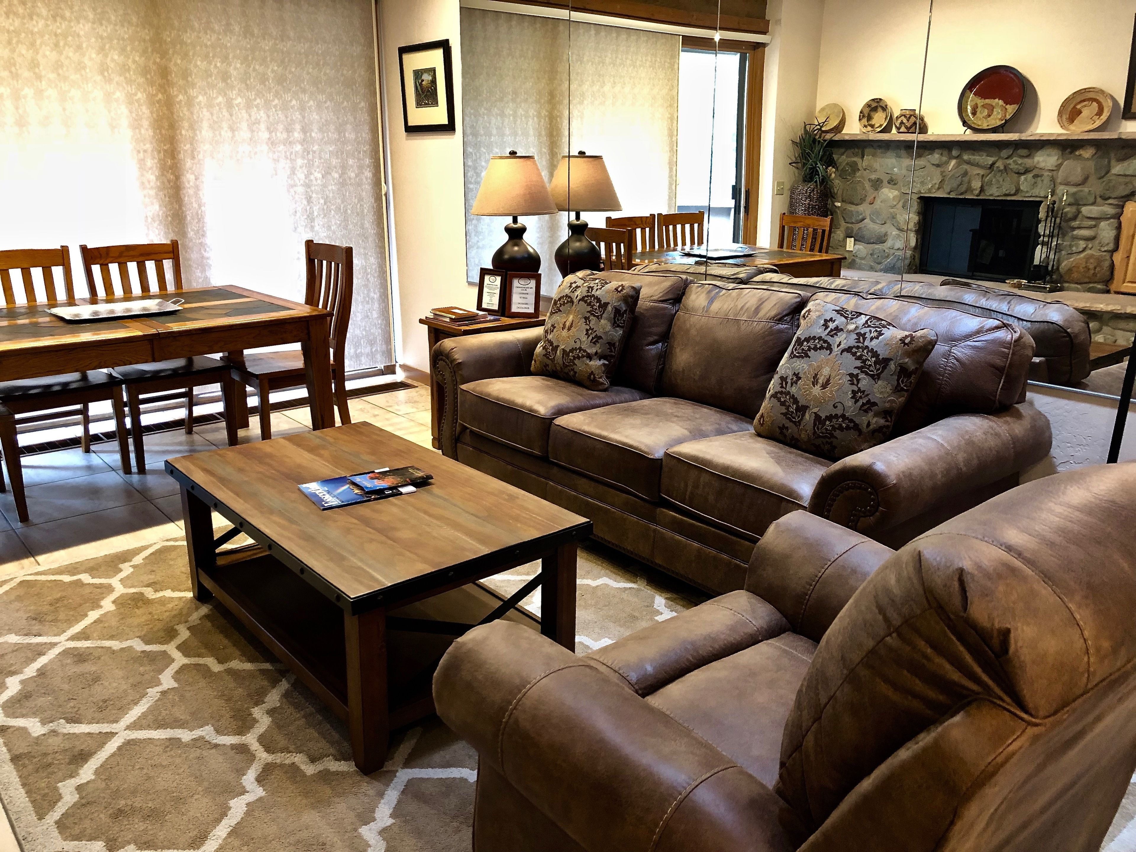 A living room with a brown leather sofa, wooden coffee table, and a dining area with wooden chairs and a table.