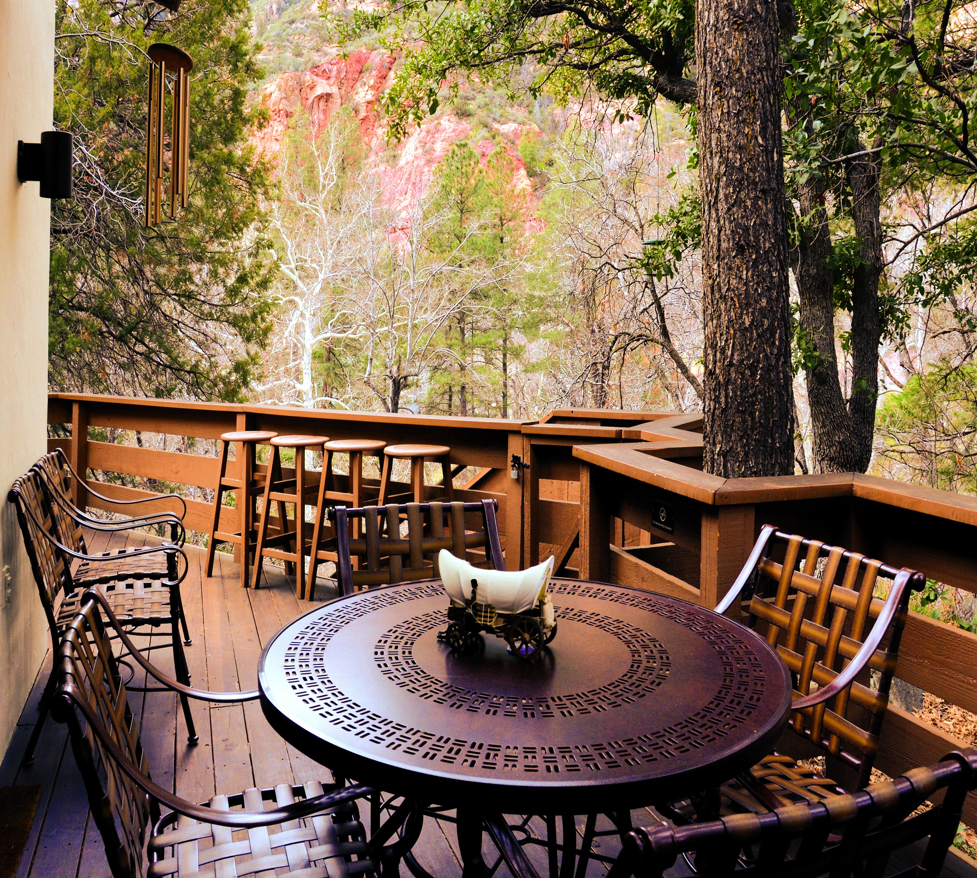 Un patio exterior con una mesa redonda y sillas, rodeado de barandillas de madera y árboles.