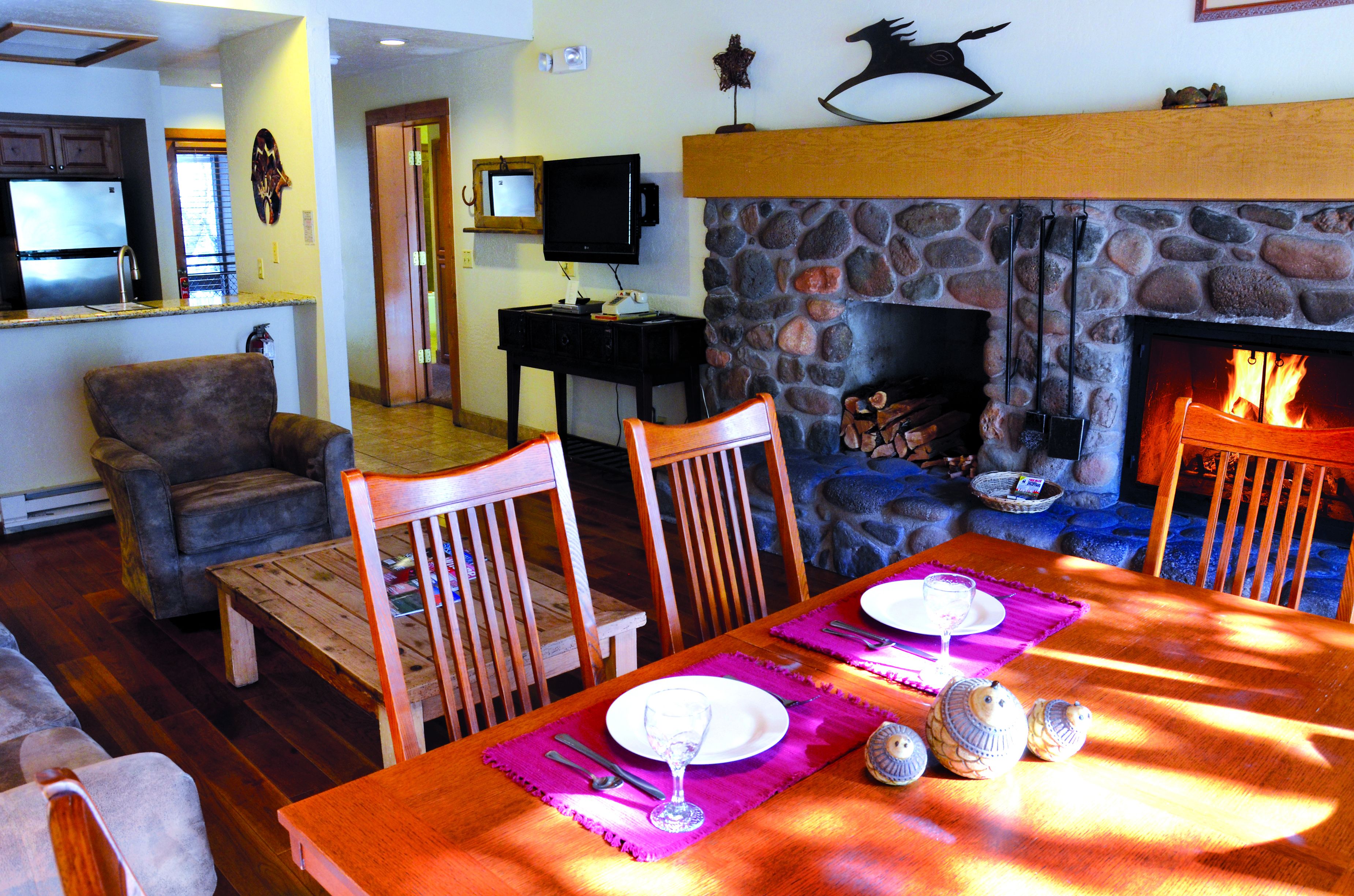 A cozy living room with a fireplace, a dining table set with plates and glasses, and a television in the background.
