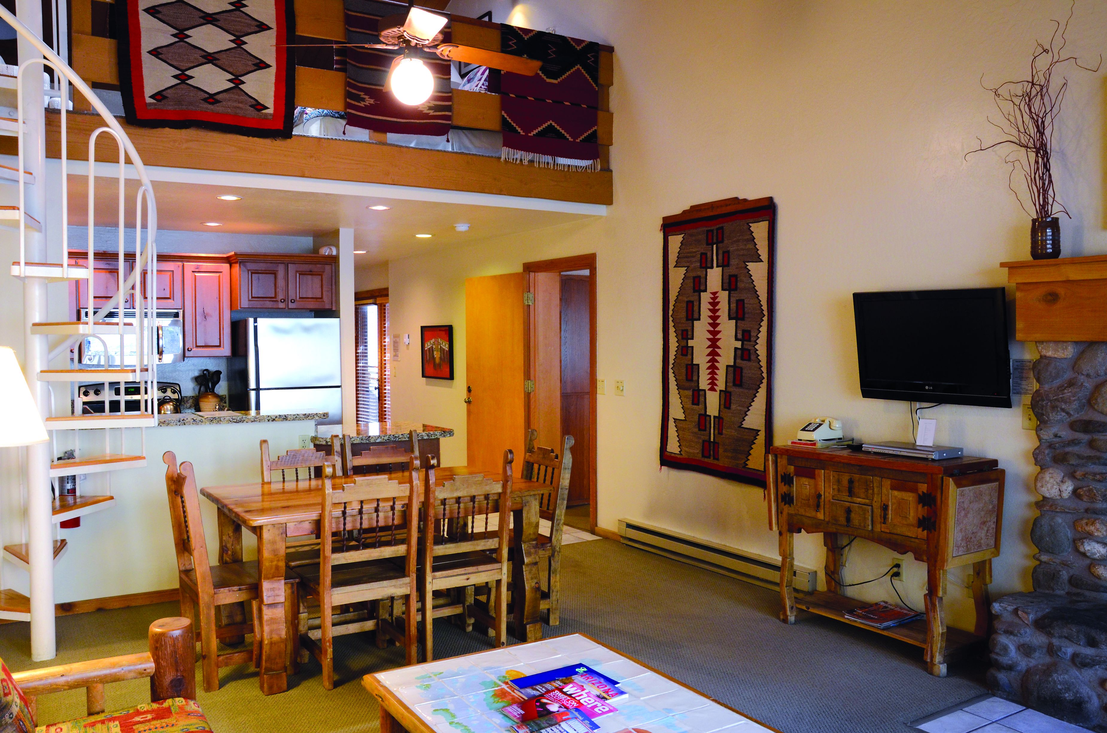 Uma sala de estar ampla com uma mesa de jantar, cadeiras, um sofá, uma TV e uma lareira.
