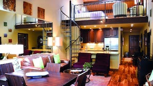 A spacious living area with a dining table, comfortable seating, a staircase leading to a loft bedroom, and a kitchen area.
