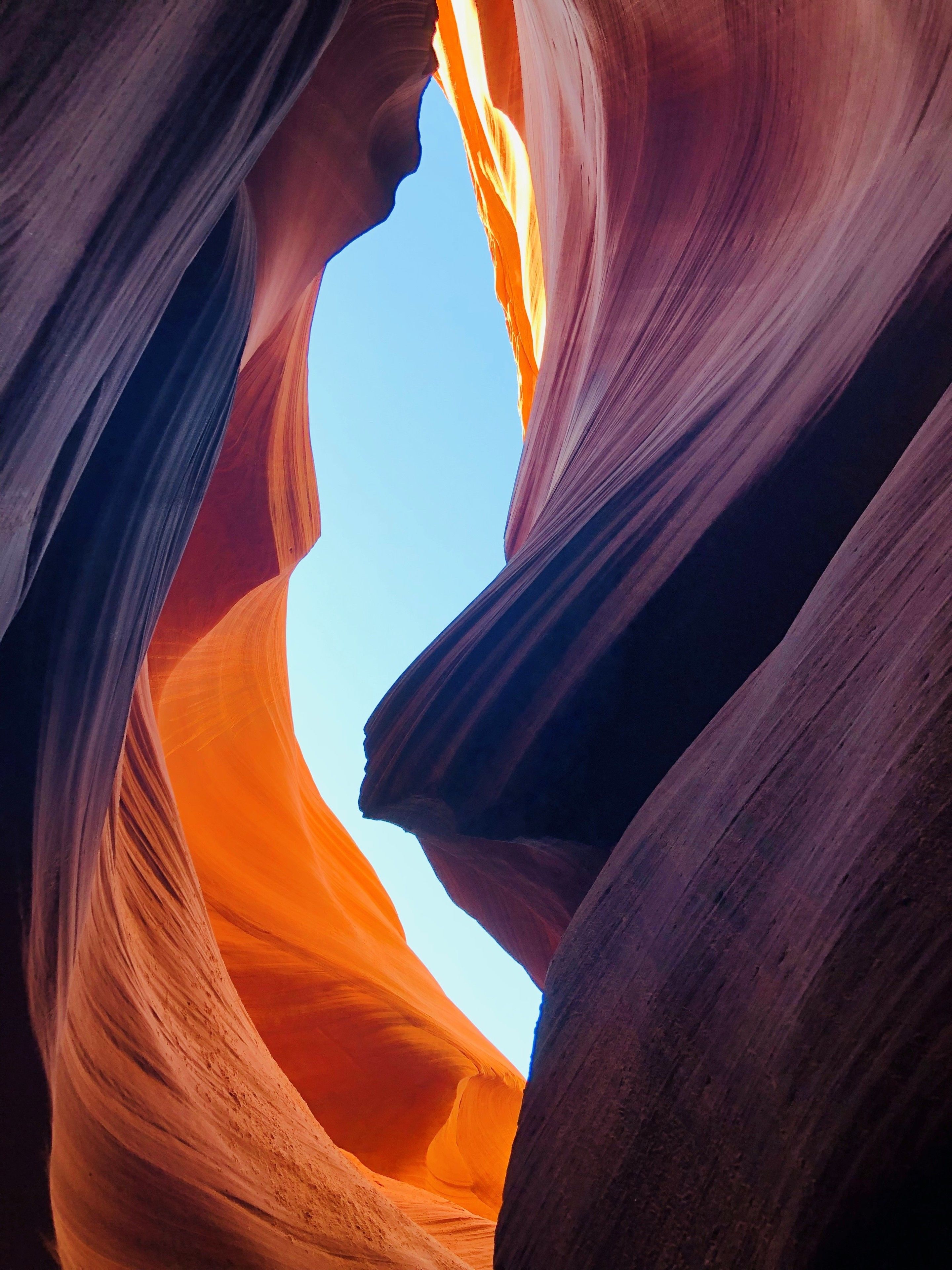 Un canyon aux parois rocheuses lisses et incurvées, et un ciel bleu clair visible à travers l’ouverture.
