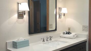 A bathroom with a large mirror, two wall-mounted lights, a sink, and wooden cabinets.