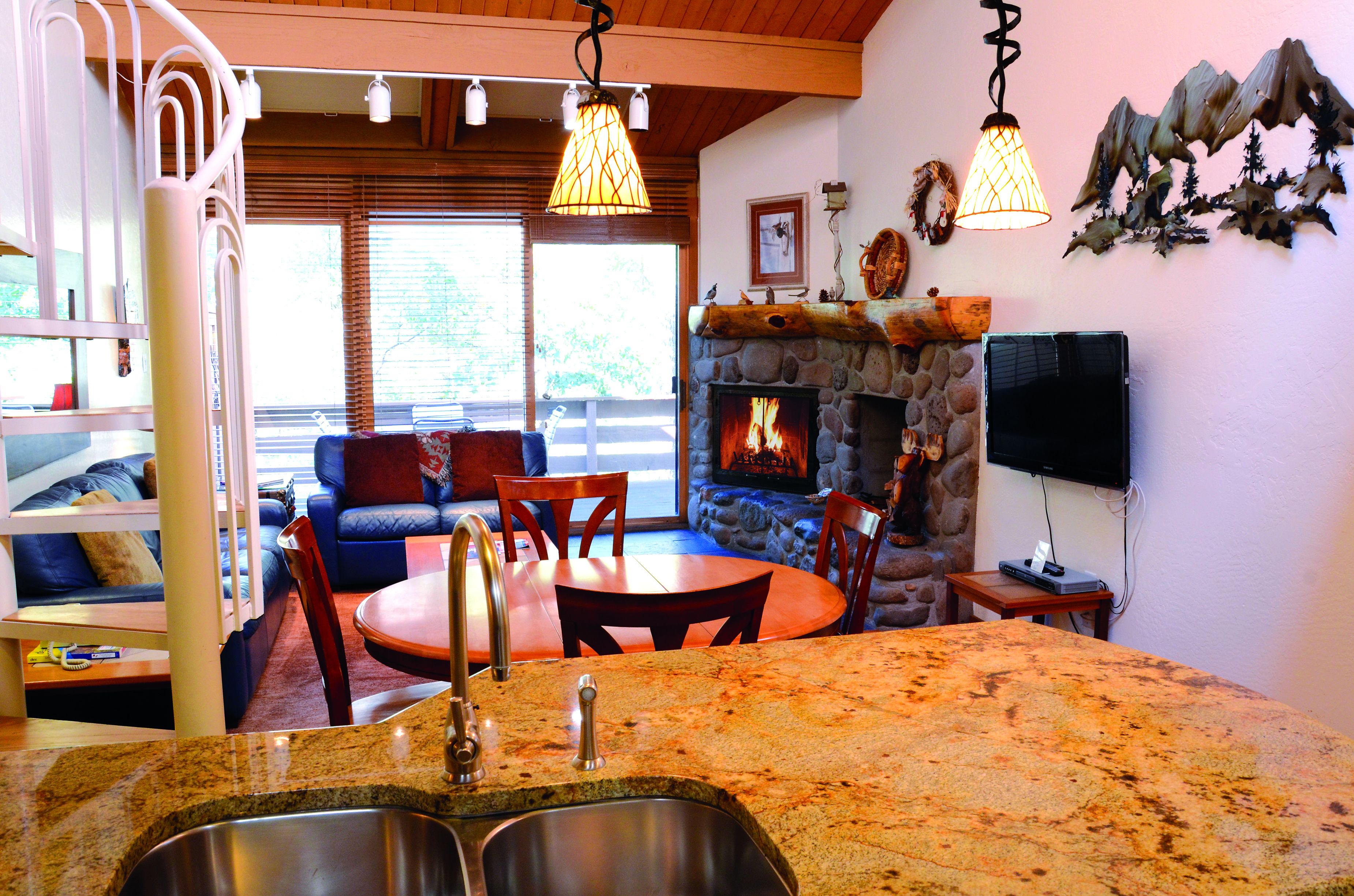 A cozy living area with a stone fireplace, wooden furniture, and a stone countertop with a sink.