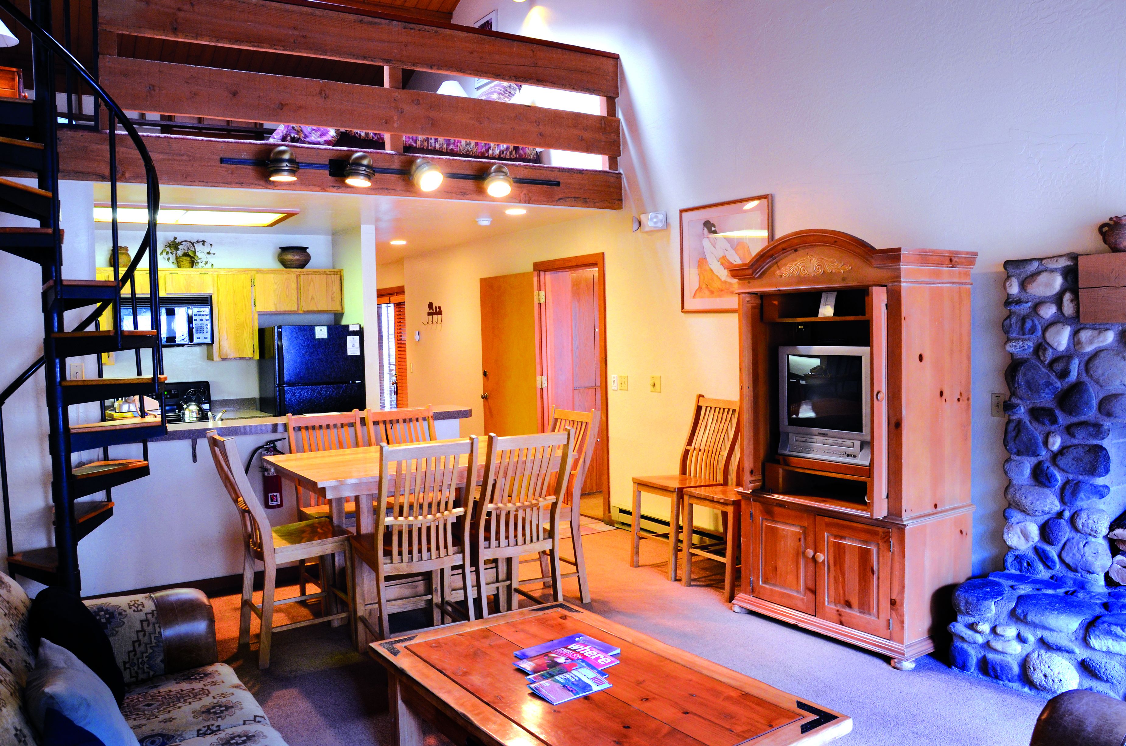 A cozy living area with a dining table, wooden chairs, a sofa, and a TV stand.