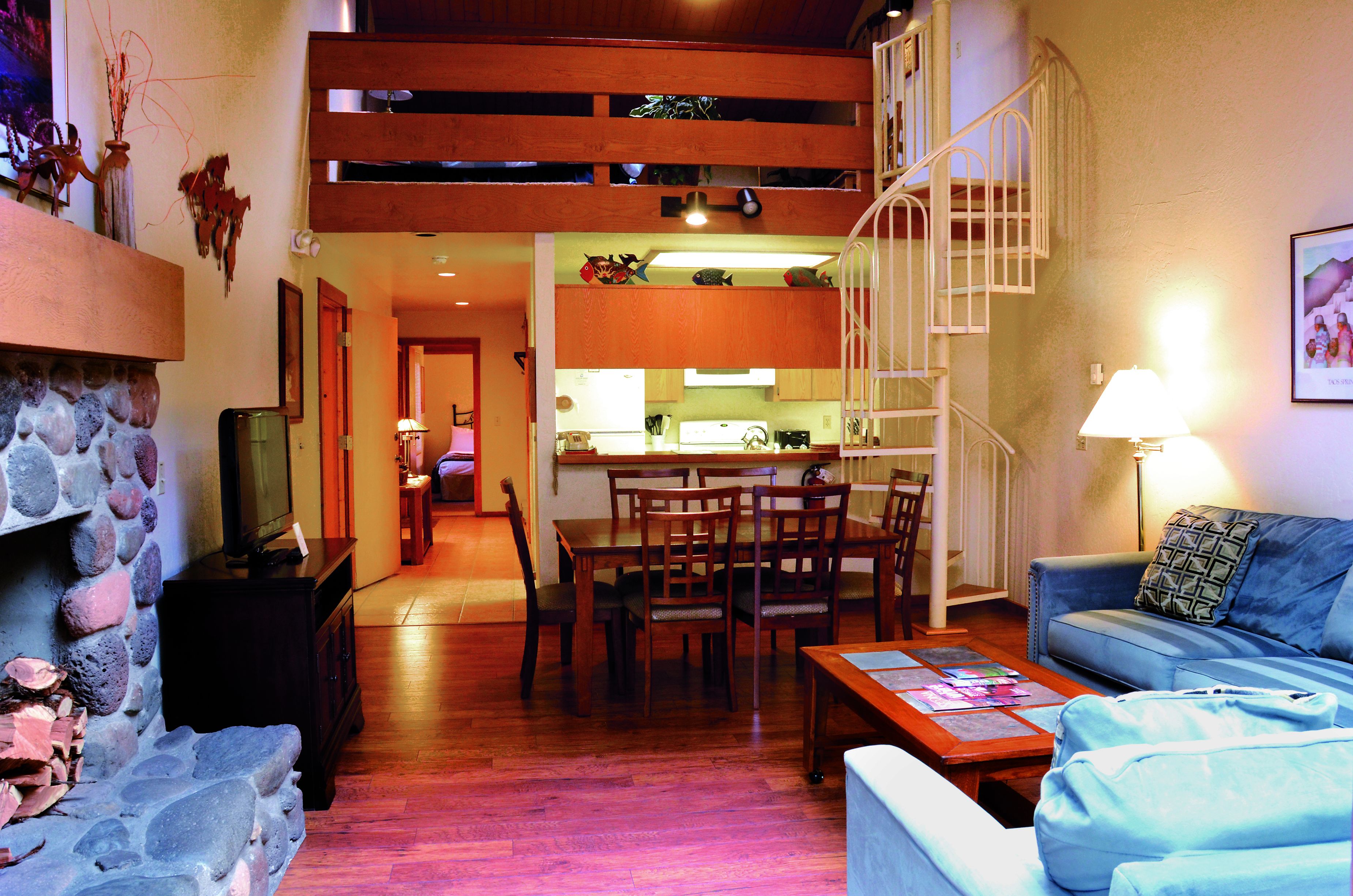 A spacious living area with a dining table, chairs, a sofa, a staircase, and a kitchen in the background.