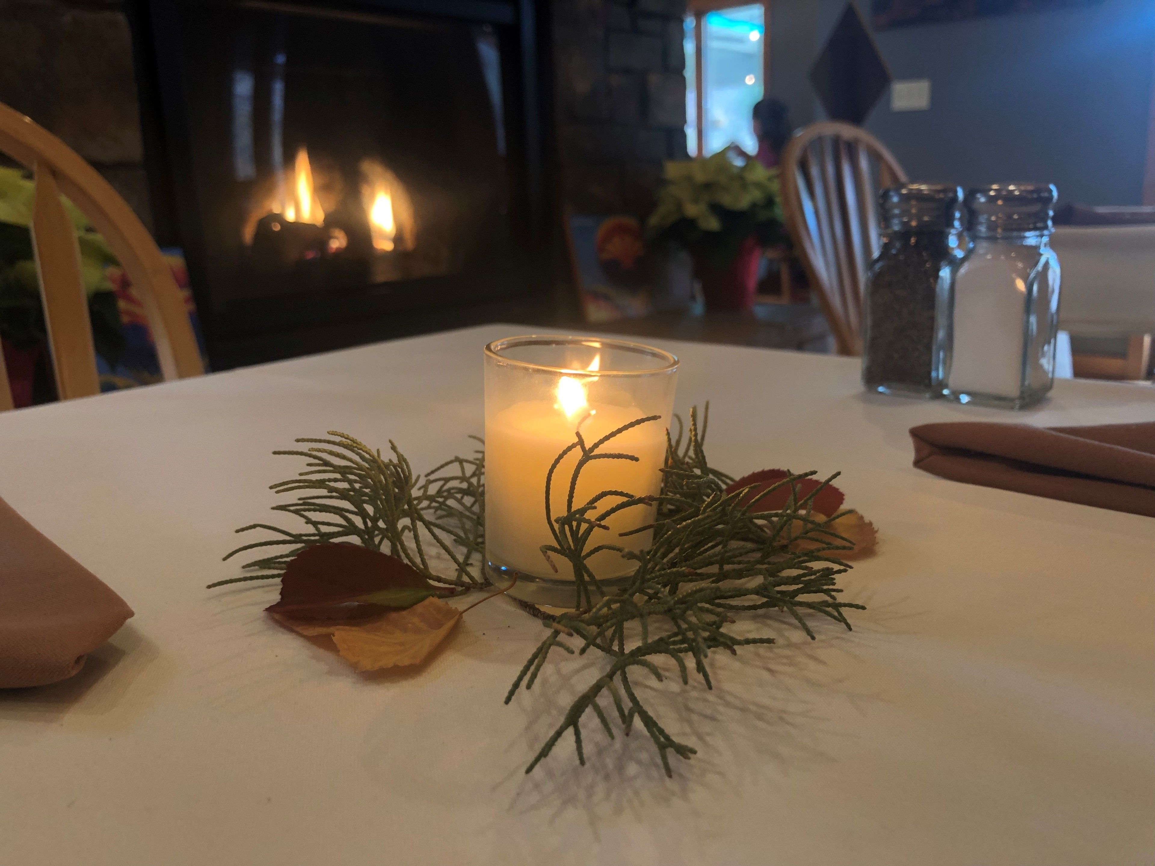 A candle on a table with a white tablecloth, surrounded by dried flowers and greenery.