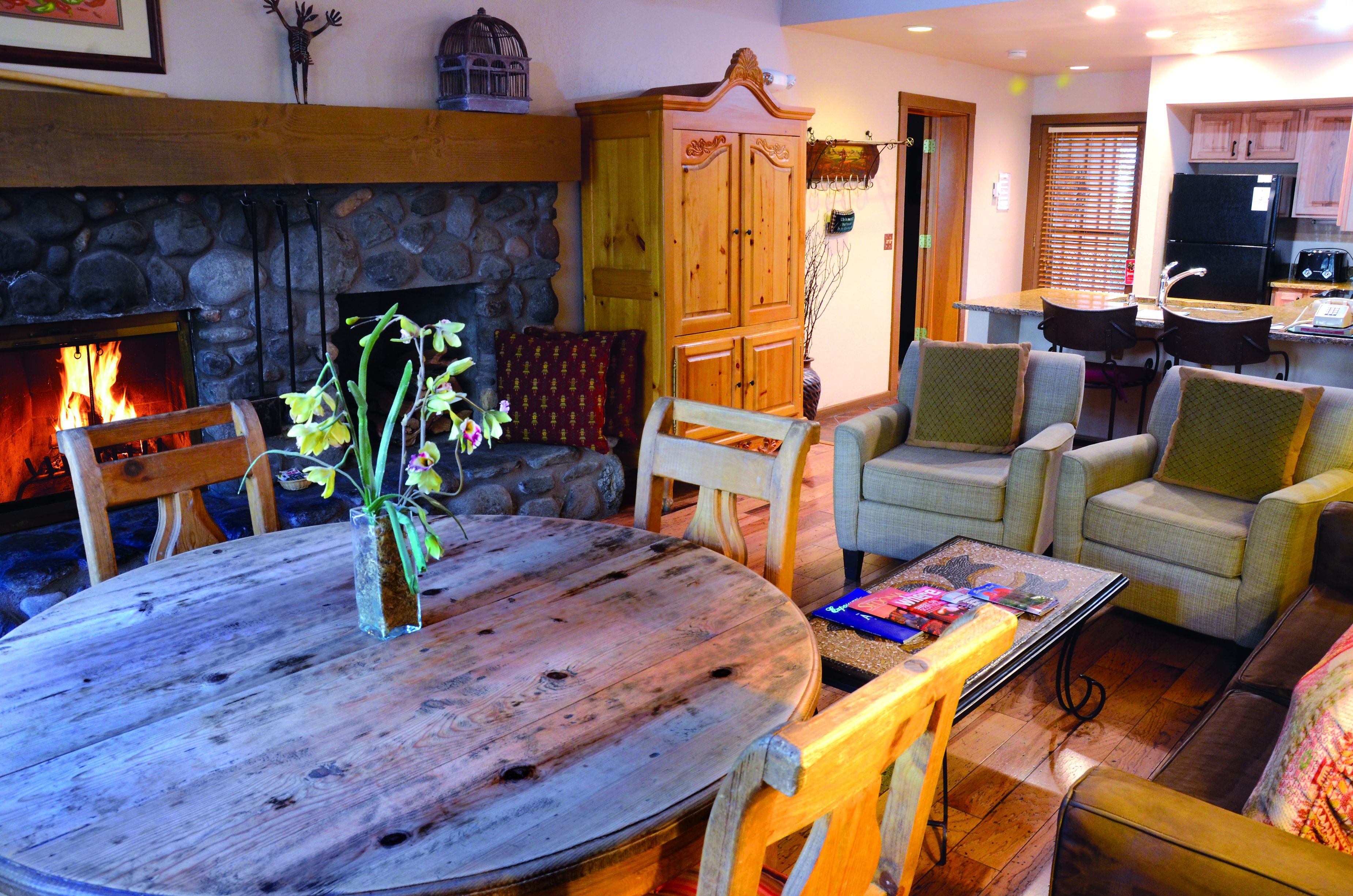 A cozy living room with a stone fireplace, wooden furniture, and a kitchen area.