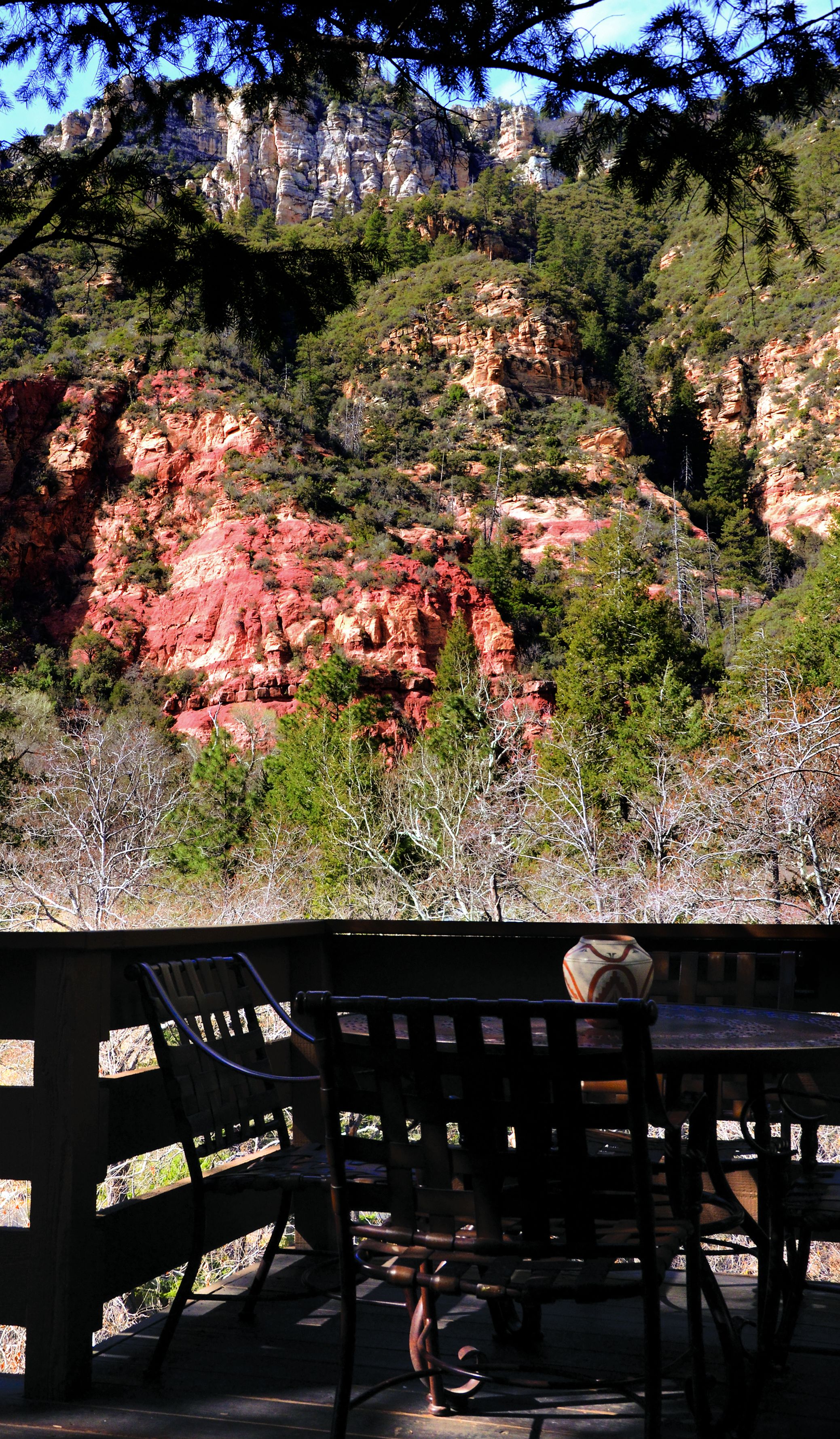A table and chairs in a shaded outdoor area with a view of red rock formations and trees.