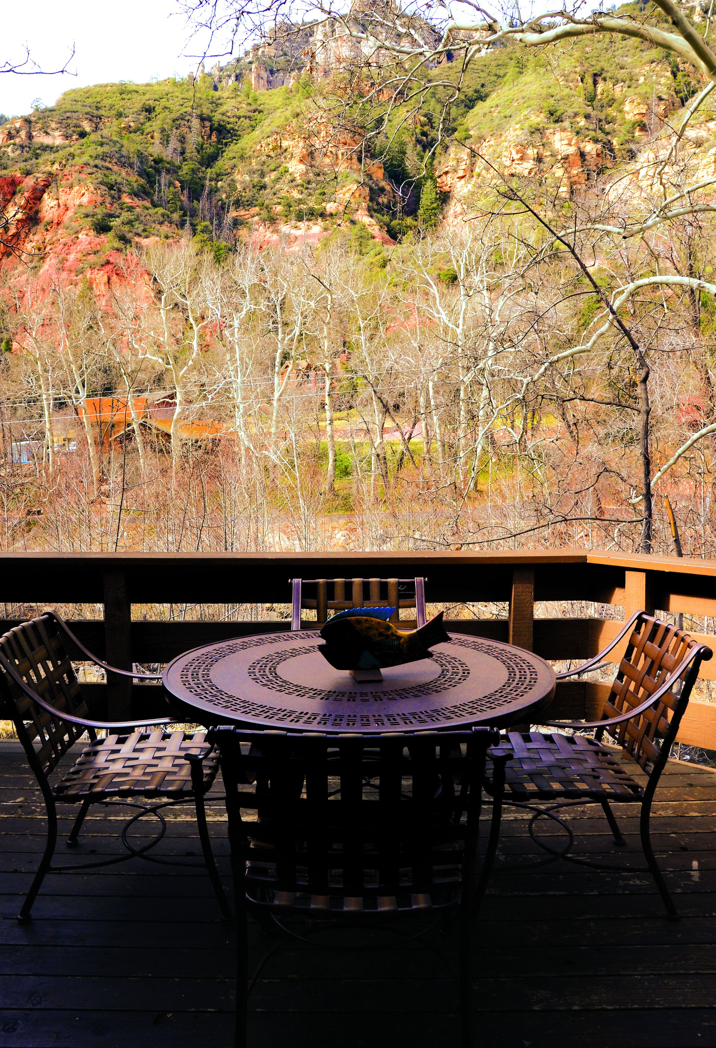 A patio with a round table and chairs, overlooking a mountainous landscape with trees and a building in the background.