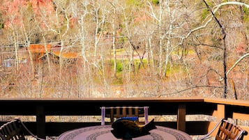 A patio with a round table and chairs, overlooking a mountainous landscape with trees and a building in the background.