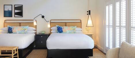 Habitación de hotel con dos camas, una mesita de noche, una lámpara, una silla y una ventana con contraventanas.