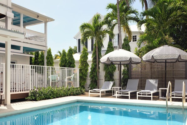 A pool area with lounge chairs, umbrellas, and a two-story building with balconies. - Winslow's Bungalows - Key West Historic Inns (Key West)