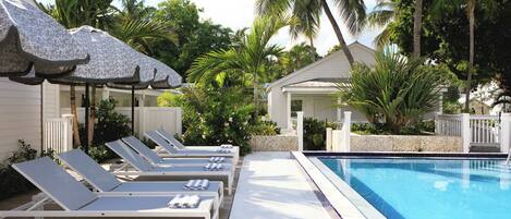 Un espace aménagé au bord de la piscine, avec des chaises longues, une piscine et une végétation tropicale.